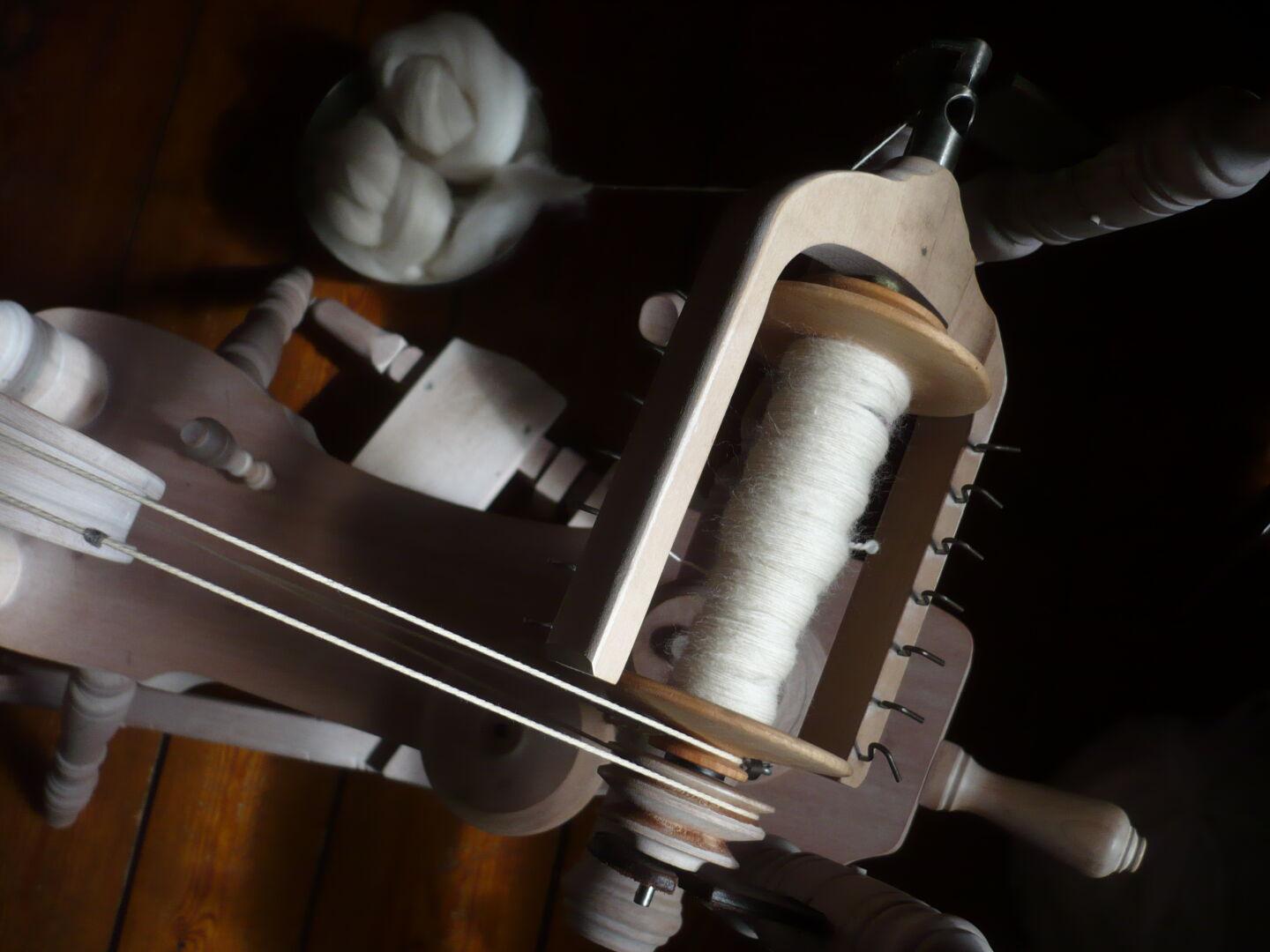 spinning wheel from above showing natural white handspun yarn on the bobbin, more fibre in the background on the floor.