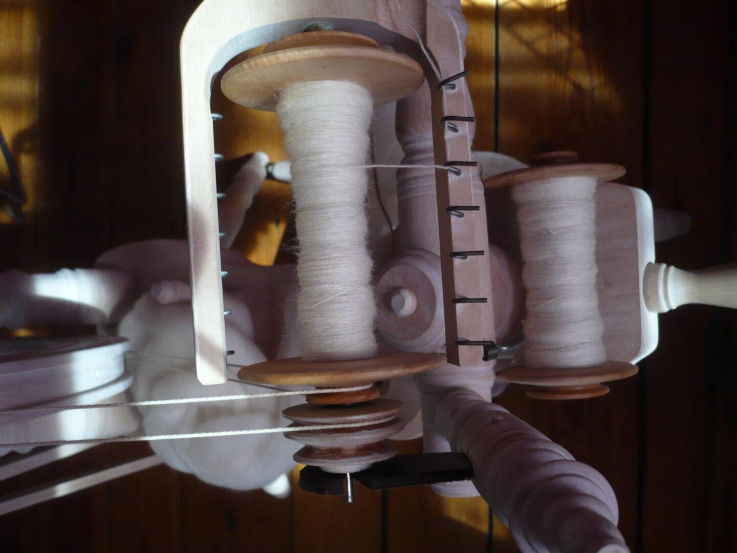 view of a spinning wheel from above, some white handspun on the bobbin, another bobbin placed below filled with white handspun.