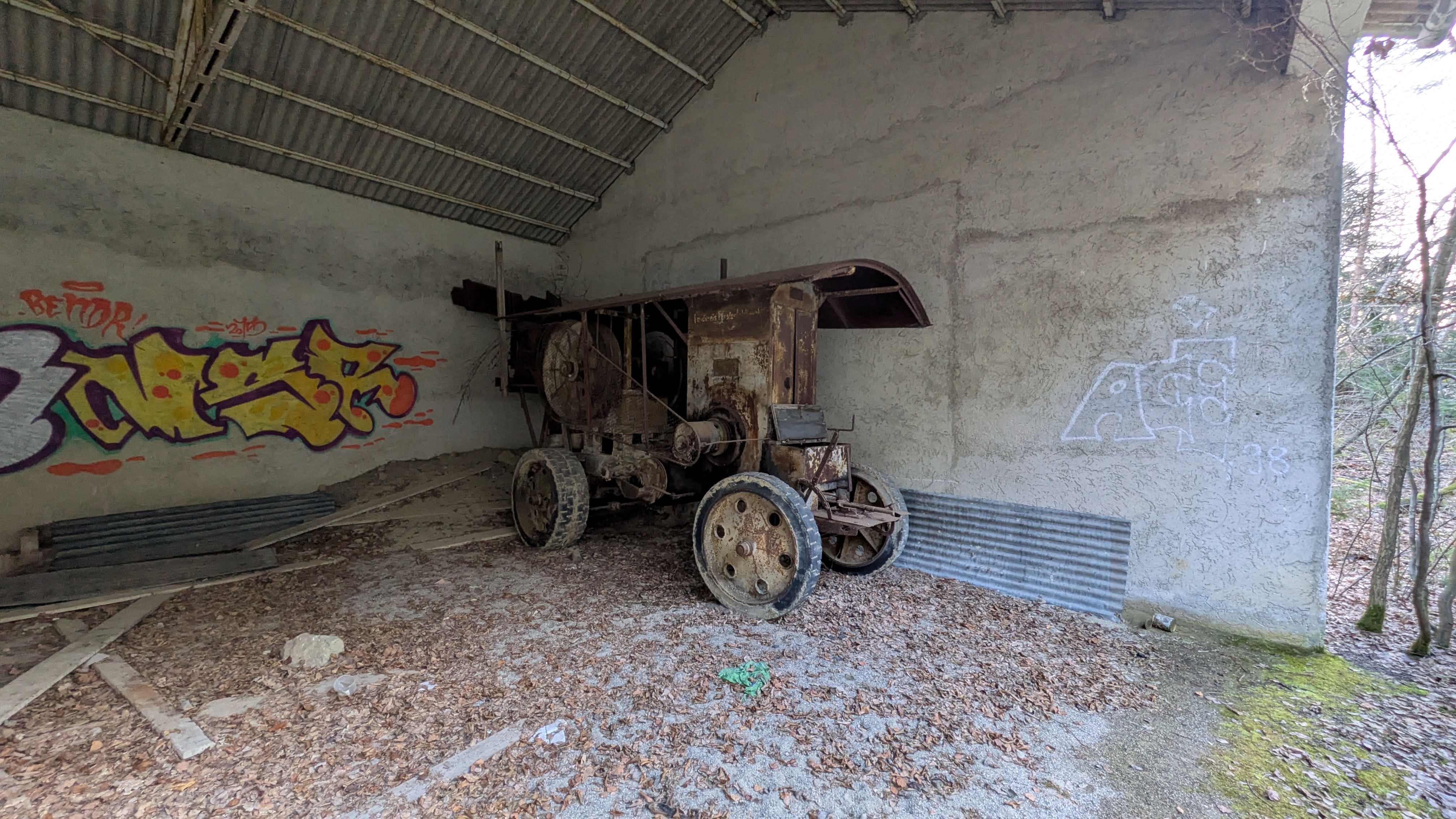 Alter, verrosteter Landmaschinenanhänger oder Dreschmaschine in einer verlassenen Halle mit Graffiti an den Wänden.