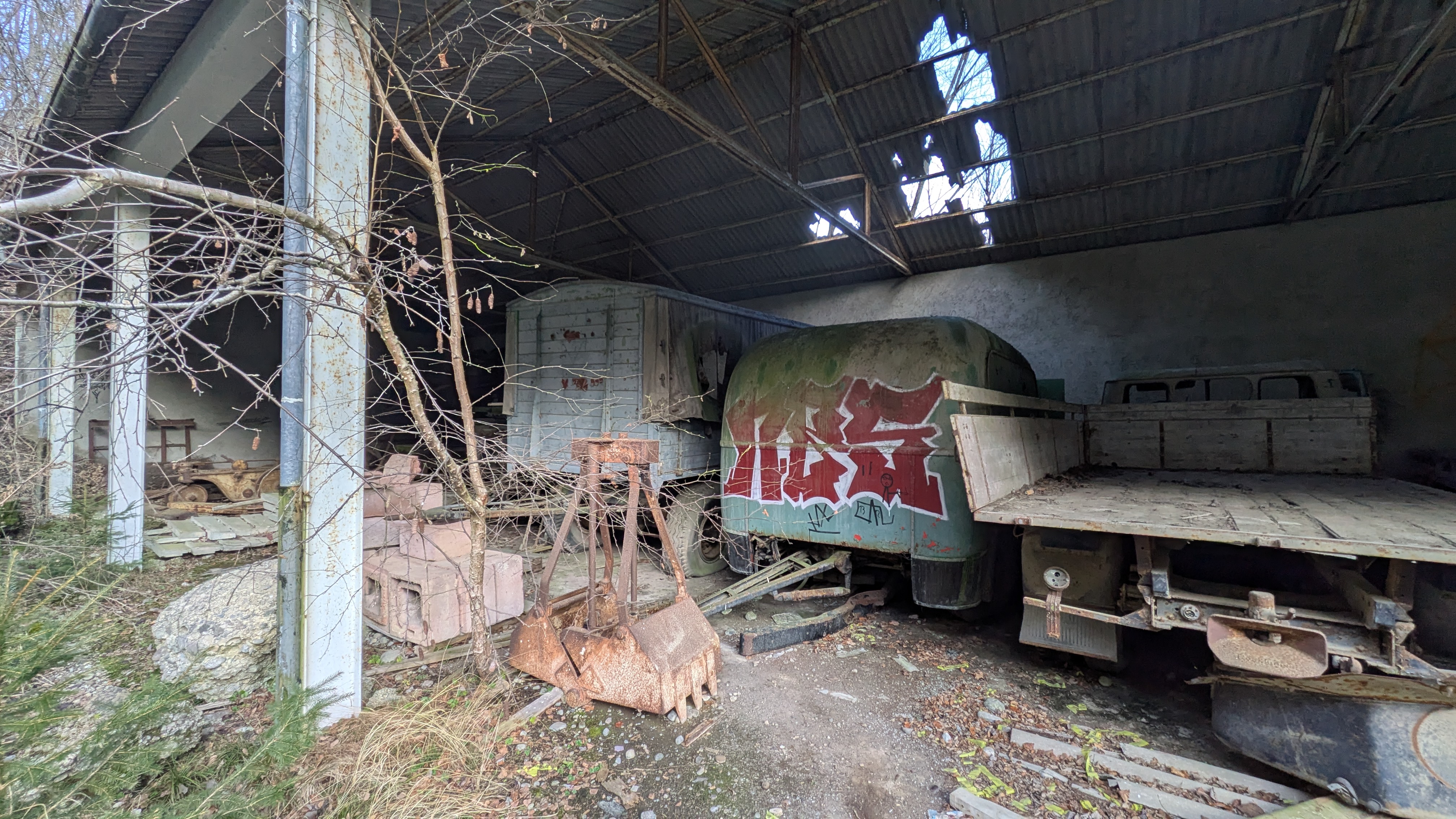 Abgestellte, stark verrostete Lastwagen und Anhänger, teilweise mit Graffiti bemalt, in einer verfallenen Halle.