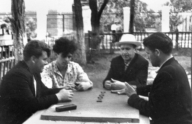 Vier Männer sitzen am Tisch draußen und spielen Domino