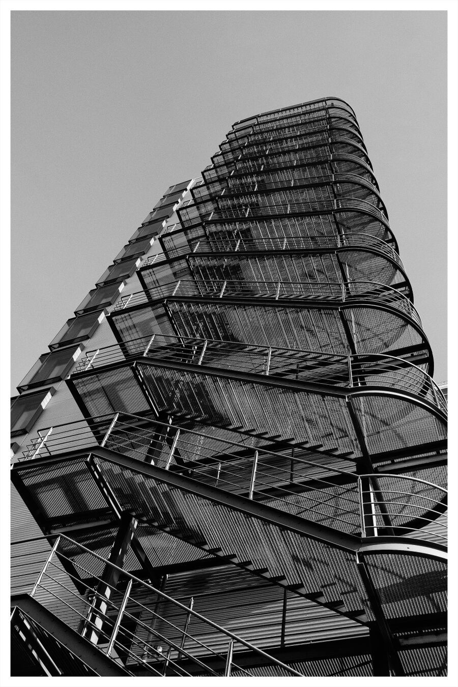 Black and white photo of an exterior spiral staircase on a modern building, showcasing geometric patterns and architectural design