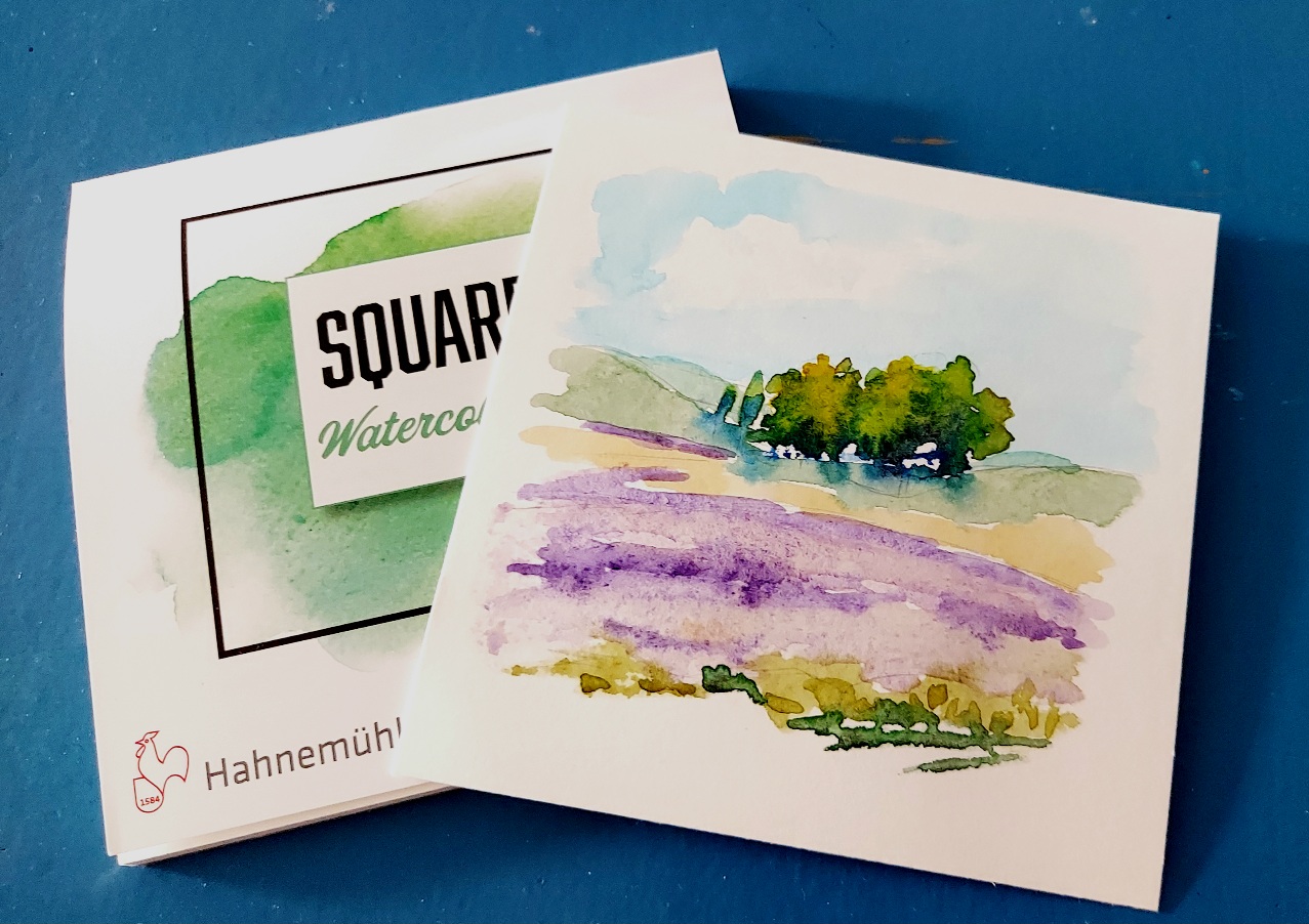 Aquarell-Landschaft mit Baumgruppe und Lavendelfeld auf einem kleinen viereckigen Aquarellblock.