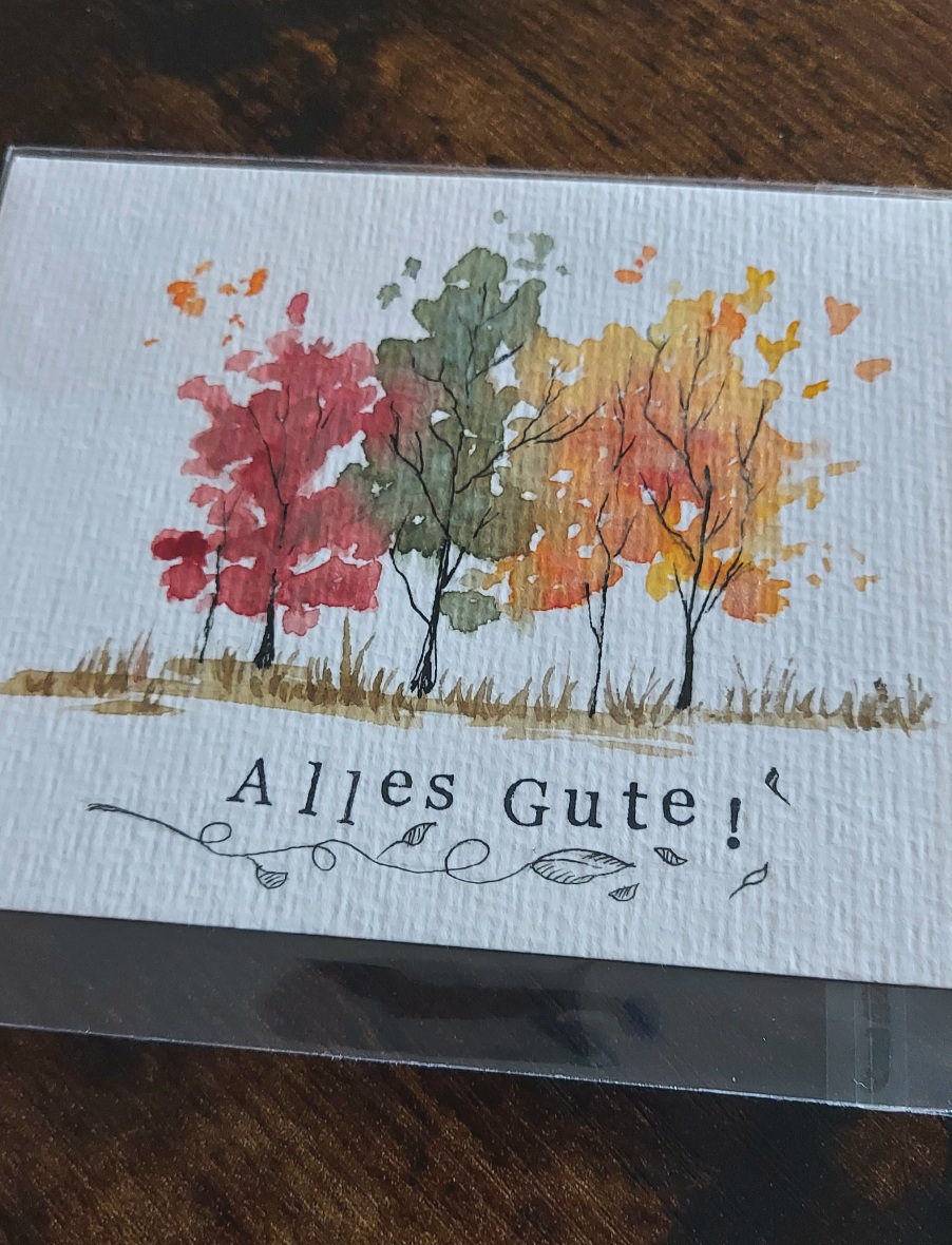 Drei Bäume in herbstlichen Farben, rot, grün, gelb. Darunter Schriftzug mit Stempel "Alles Gute".