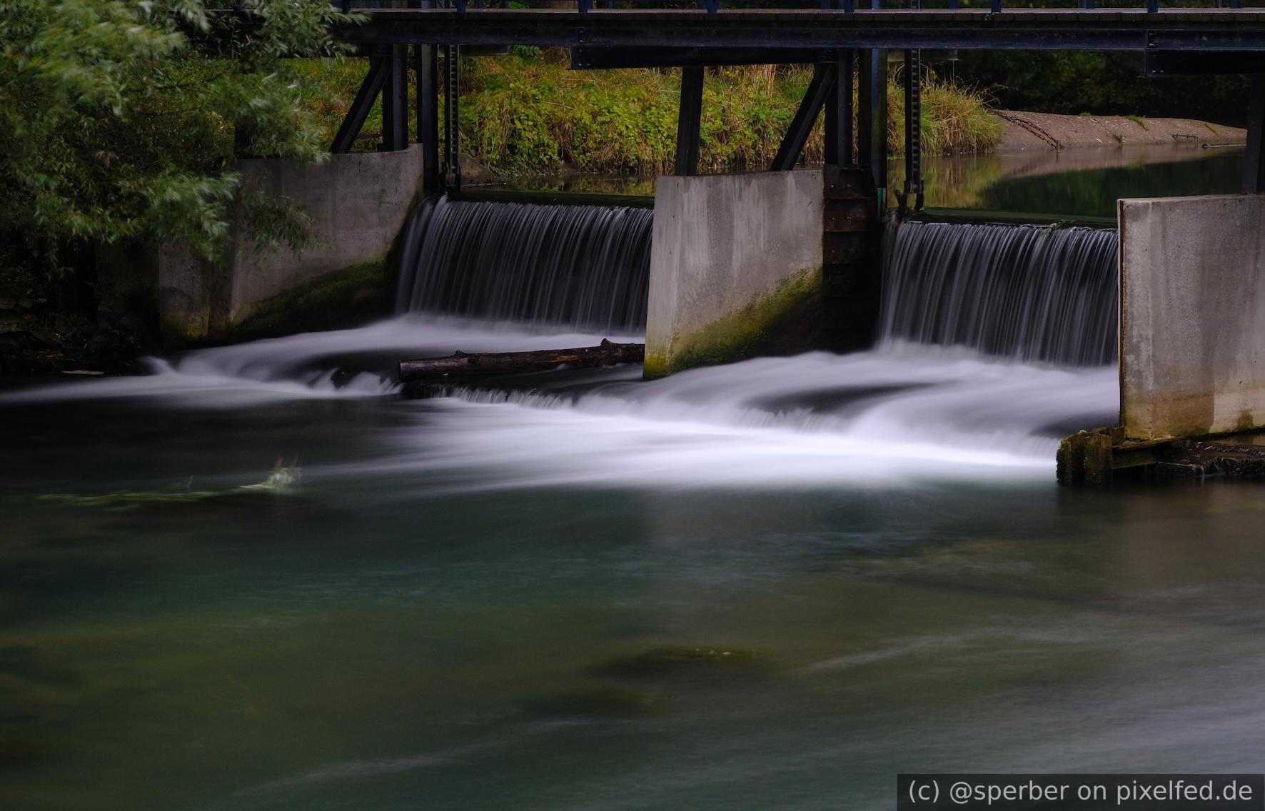 River flowing over a small dam under a bridge. The water looks smooth, due to the long exposure time.