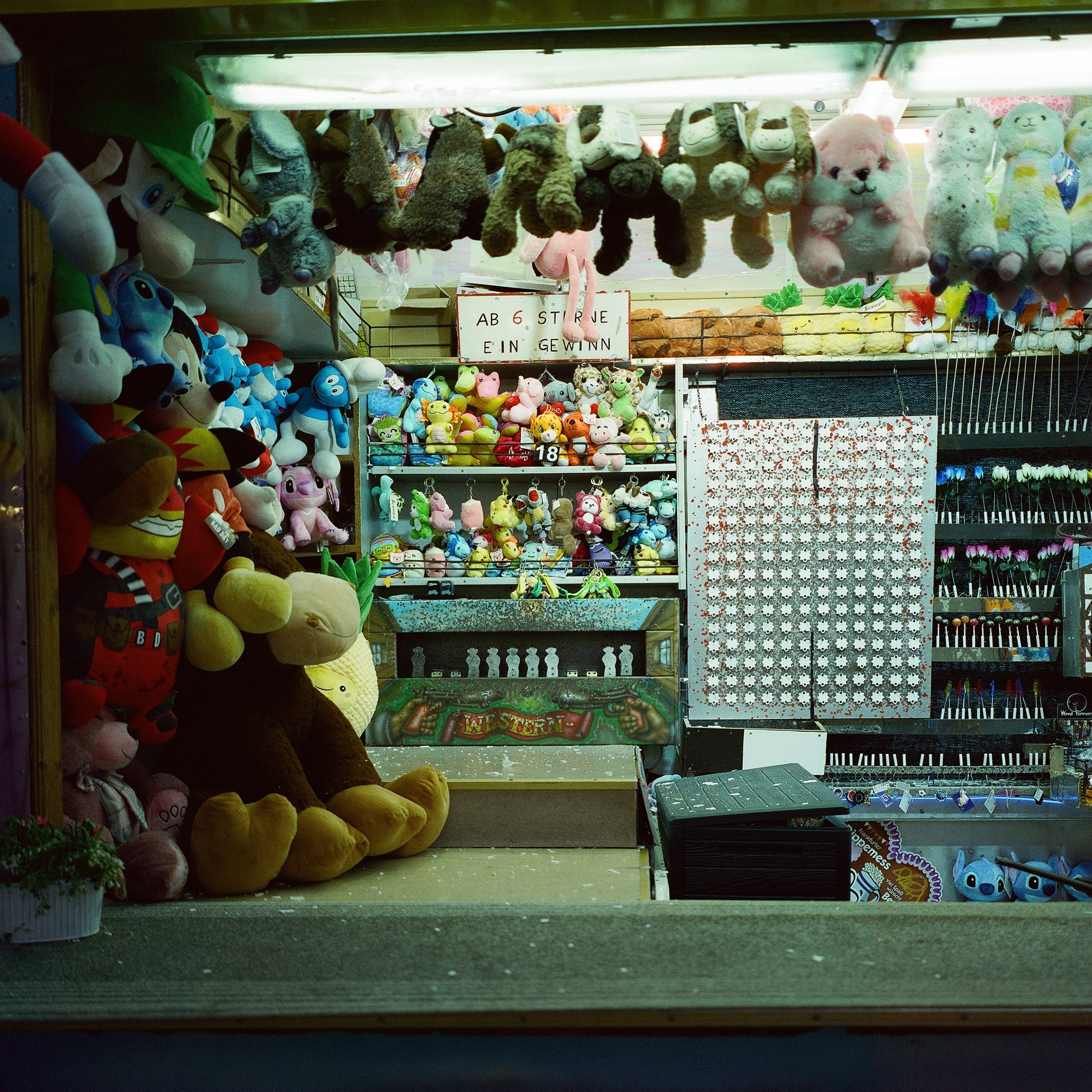 A photo of a fair stand, a shooting game where you have to hit 6 targets to win. On the left and in the middle are the plushie prizes.