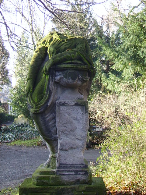 alter bemooster Grabstein mit Figut ohne Kopf