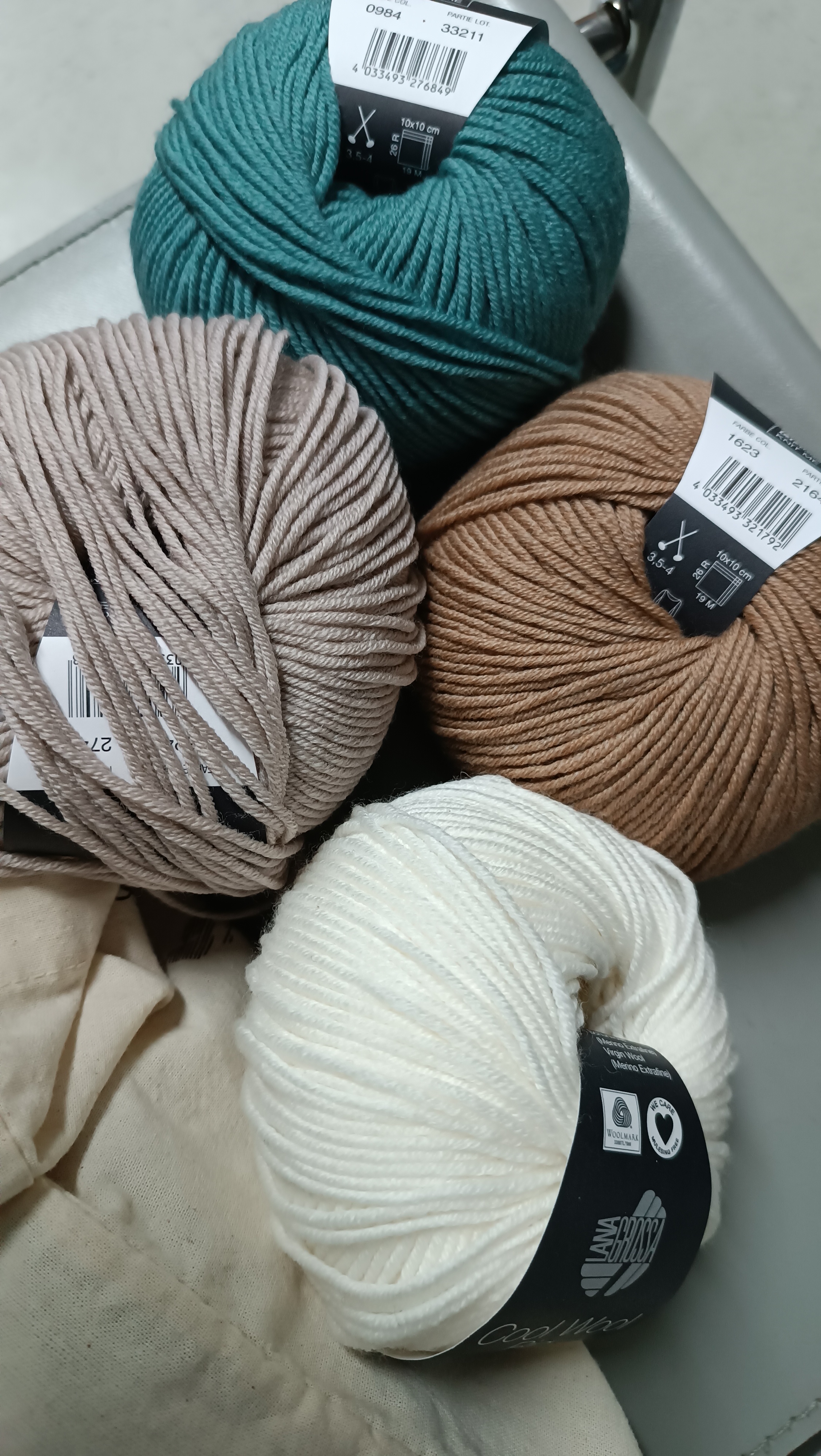 4 balls of yarn with following colours starting from the top, then clockwise: petrol, light brown, natural white, beige.