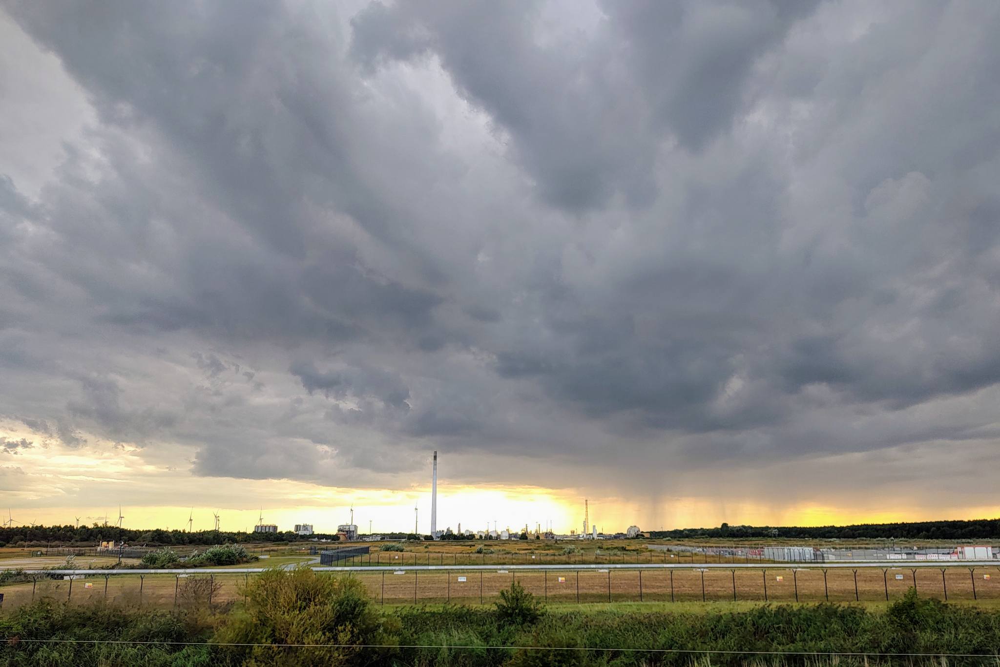 industrial complex, Wilhelmshaven, with mighty clouds and visible downpours above and the setting sun in the background