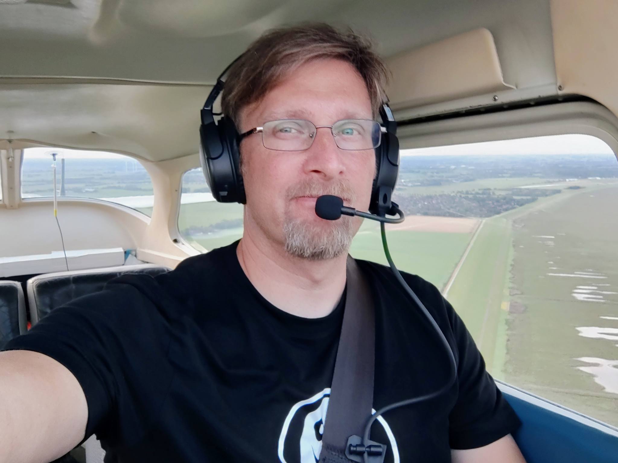the pilot seen in the cockpit of a Cessna C172 flying at 800 ft; he's wearing a black headset and a black T-Shirt with the Filmation Ghostbusters Ghost logo