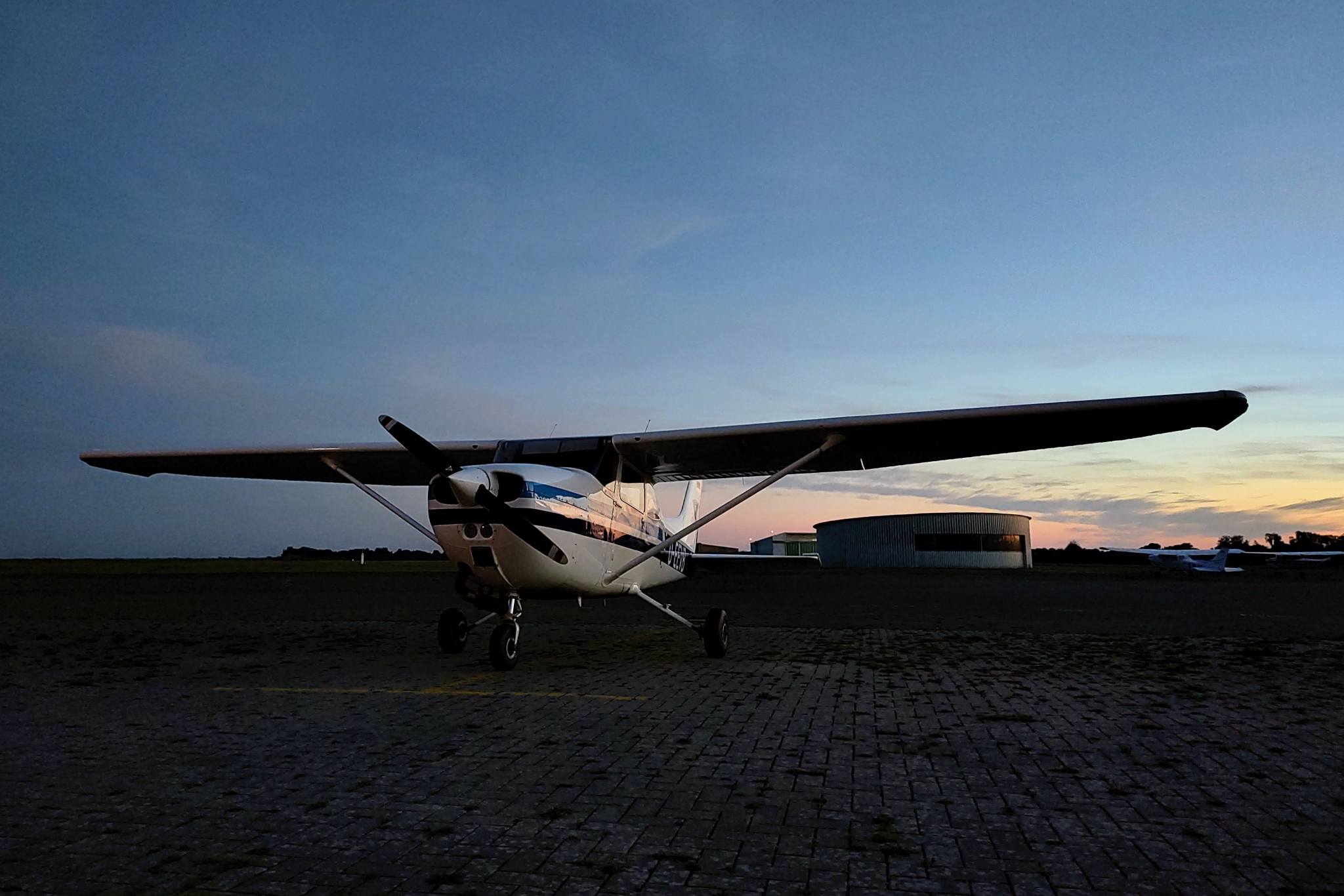 Cessna C172 light airplane standing on the apron, facing the camera slightly to the left, with the setting sun to the right