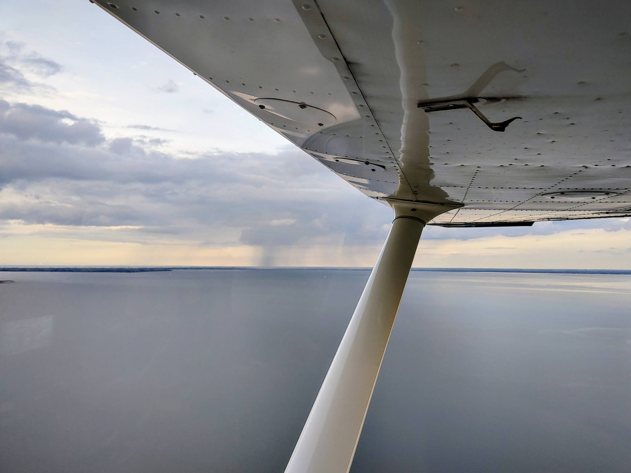 view from the cockpit of a Cessna C172 flying at 800 ft, along the right wing; in the distance a cloud with rain is visible, down below is the Jade bight
