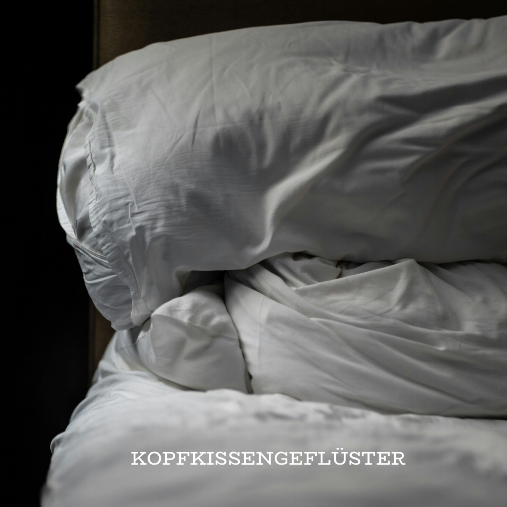 Nahaufnahme eines ungemachten Betts mit weißen, zerknitterten Kissen und Bettdecken in weichem, seitlichem Licht. Links ist der Hintergrund dunkel, rechts begrenzt ein Polster oder Kopfteil den Bildausschnitt.