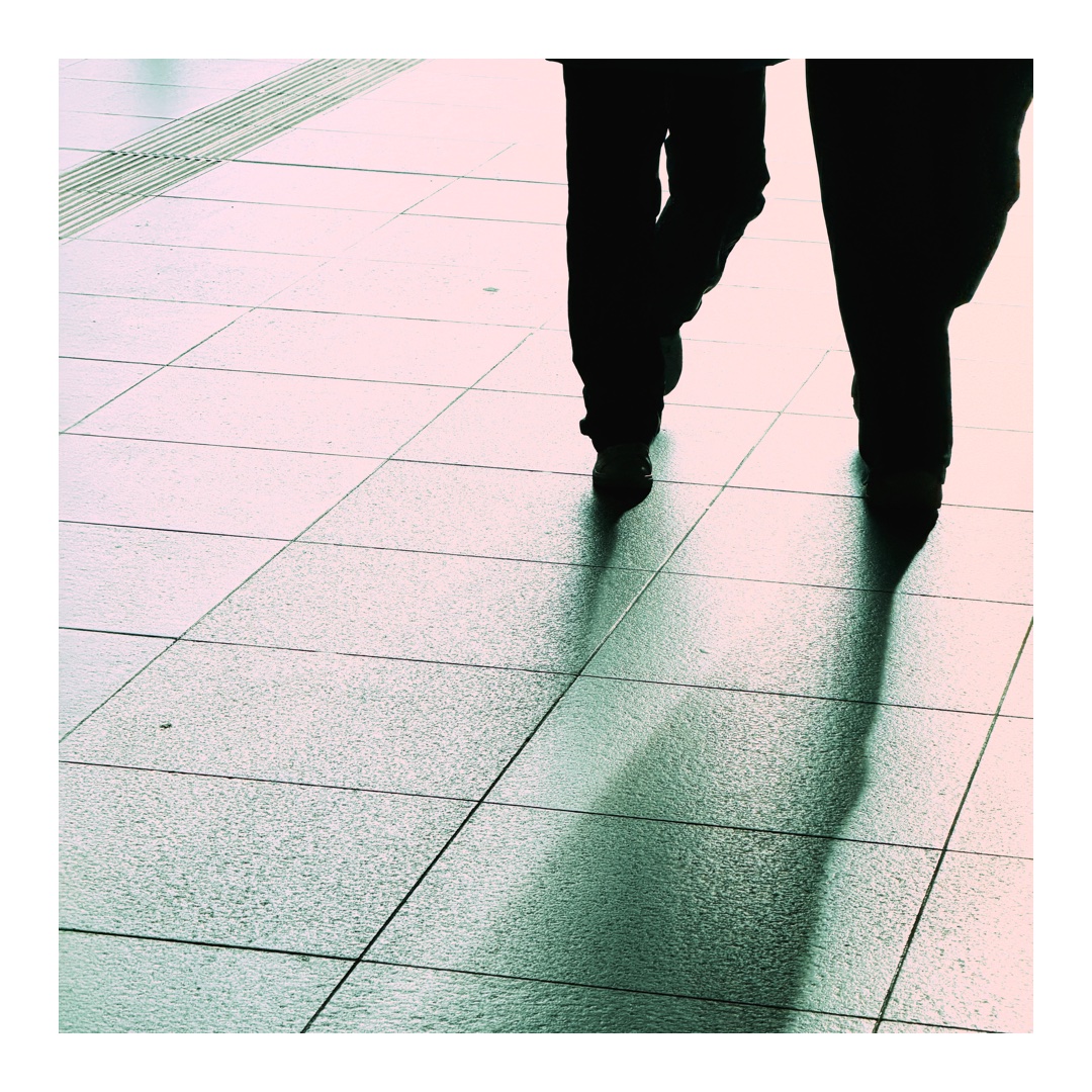 Beine und Hüfte zweier gehender Personen im Gegenlicht auf glattem Boden mit Schatten