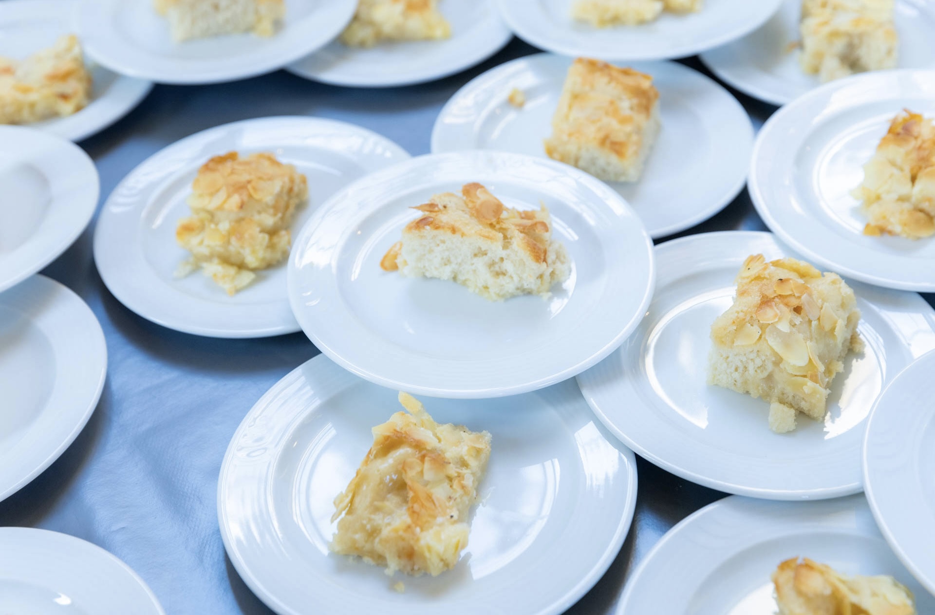 Viele Teller nebeneinander und über Eck gestapelt mit jeweils einem kleinen Stück Butterkuchen darauf.