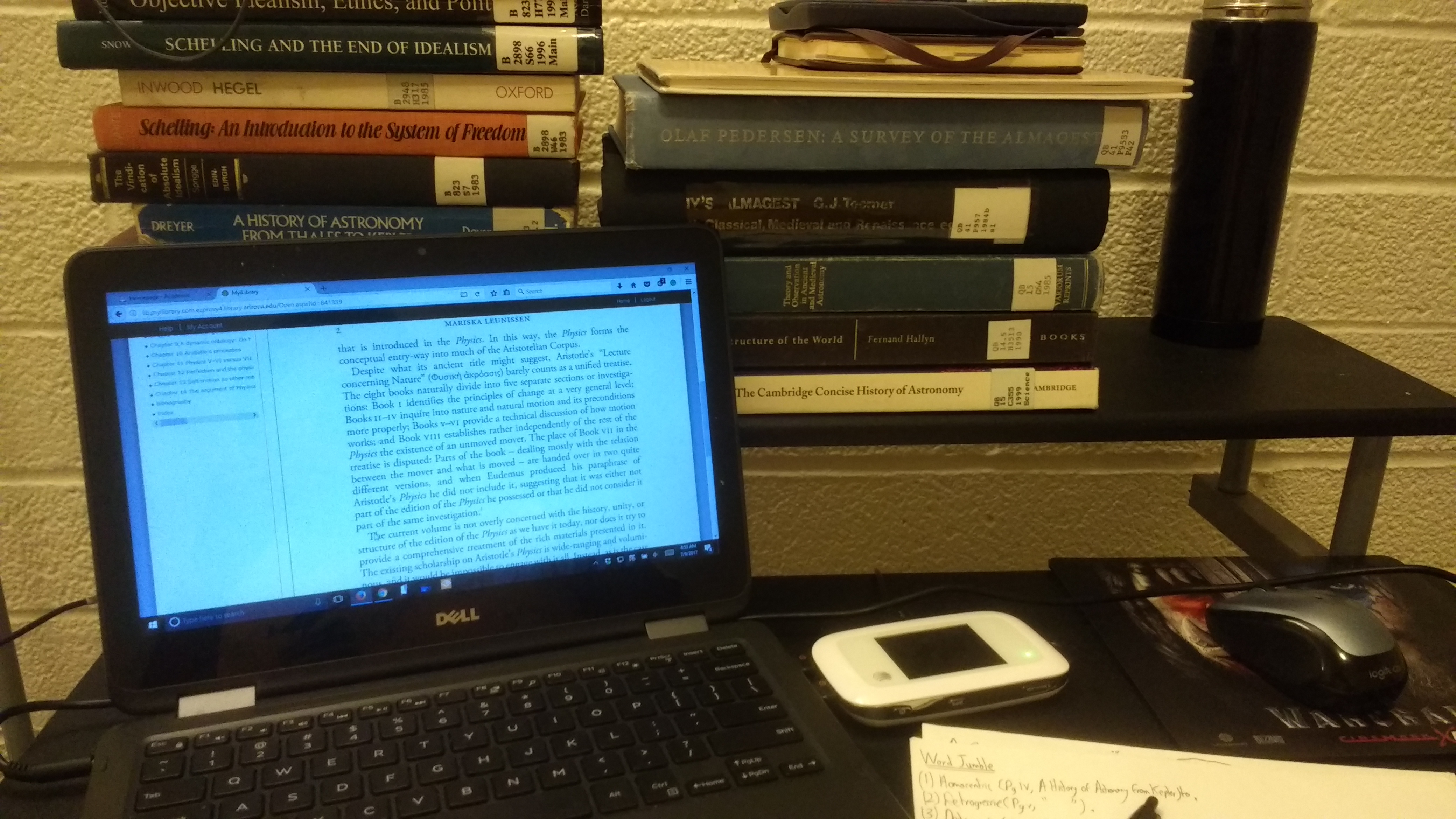 A small table, fit for one person. A small 11 inch laptop on the left side, with the mouse and a small piece of paper on its right. On the upper layer of the table, there are 2 rows of books. One row contains books written on Schelling, a german idealist during the post-medieval era. the other row contains various other books of similar value.