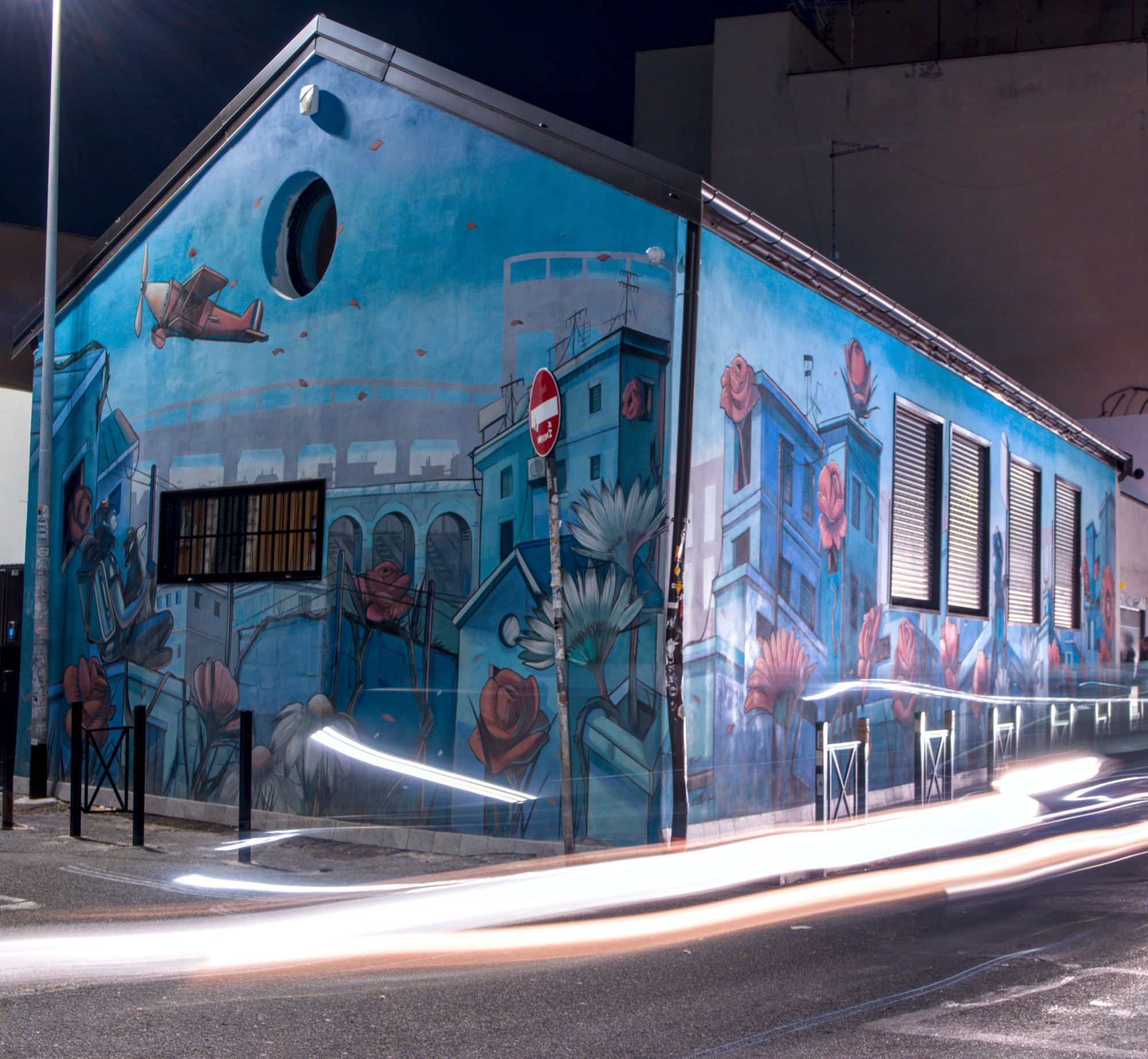 Long exposure pic of a blue house, there are some car leaving light waves