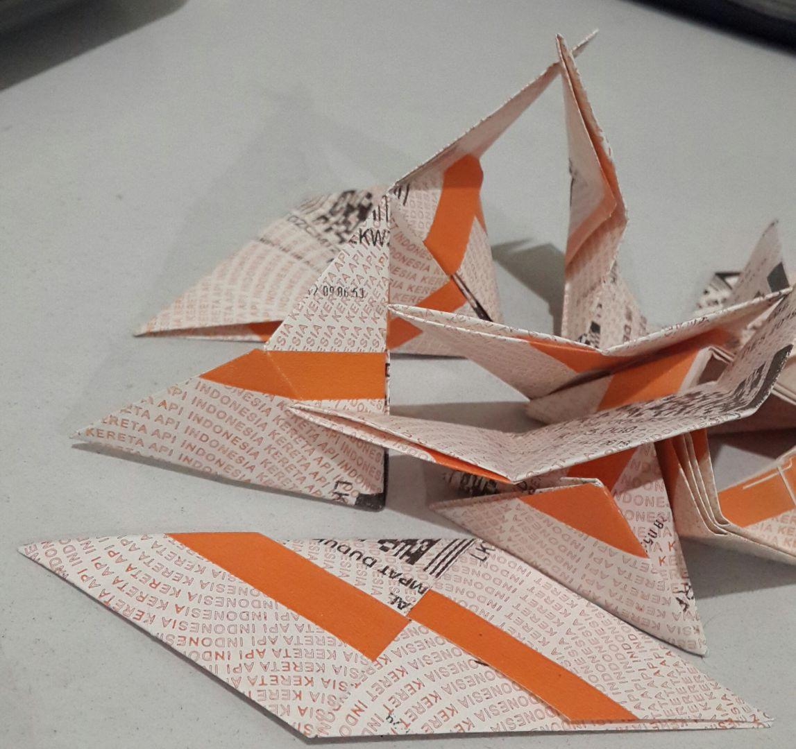 A bunch of few sonobe origami units, each folded from an orange and white train ticket stub.